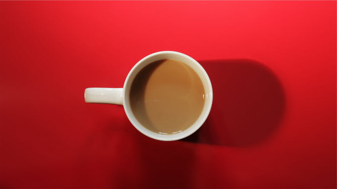 An overhead view of a cup of coffee on a red background.