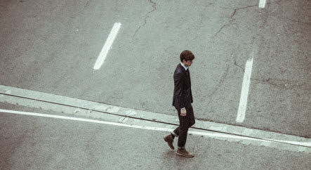 A man wearing a suit walks across an empty city street.