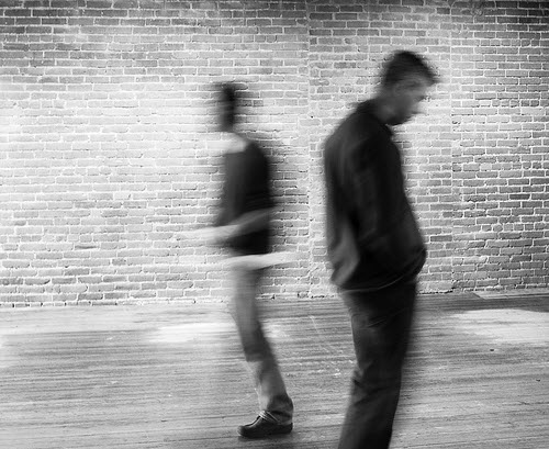 A black and white image of two men, blurred, in front of a brick wall.