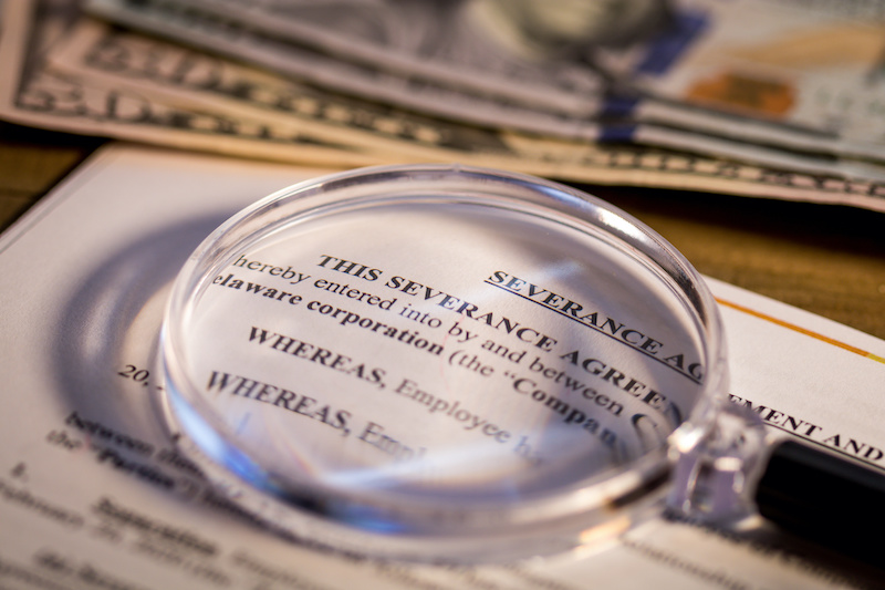 There are common questions about severance pay, as represented by a magnifying glass highlighting a severance agreement.
