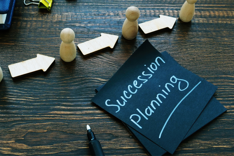 Succession Planning written on a note on a desk covered with figurines and arrows representing succession