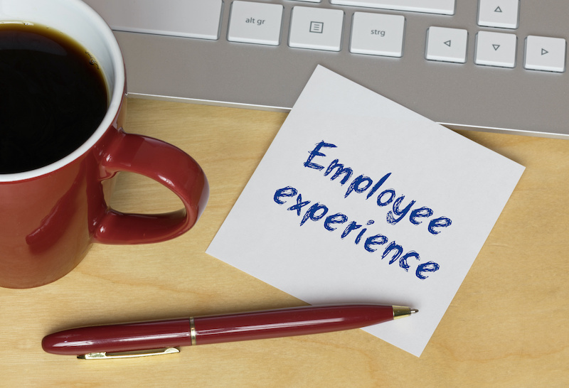 A note reading "Employee experience" sits atop a desk by a keyboard, pen, and mug of coffee.