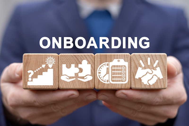 A businessman's hands hold blocks showing symbols of onboarding with the word ONBOARDING above them.