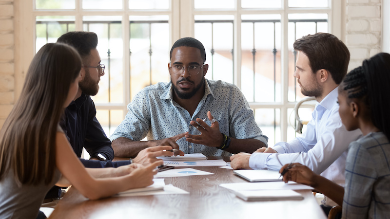 An African-American male manager meets with a small group of employees to discuss how he can support remaining employees after a layoff