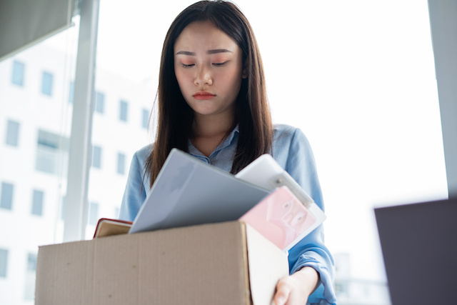 Young Asian woman looks depressed as she stands with her belongings from work boxed up after being laid off.