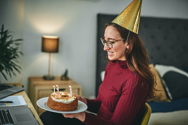 A female remote employee participates celebrates her birthday virtually with her colleagues from her desk at home