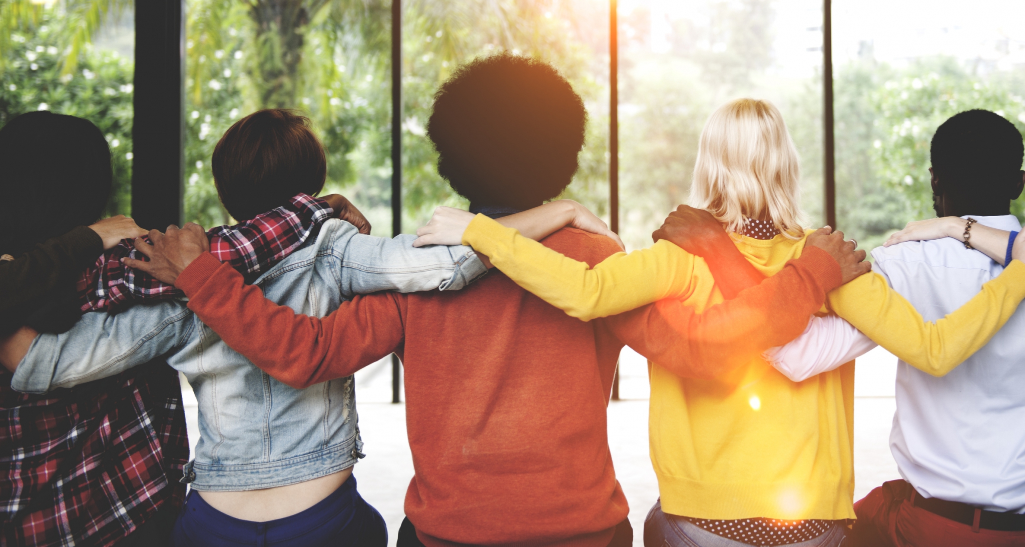 A diverse group of people sitting with their back to the camera and arms around one another