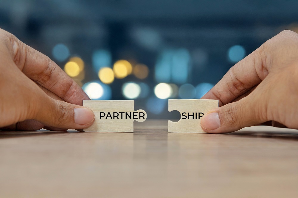 Two hands holding two puzzle pieces to form the word PARTNERSHIP.