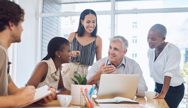 A young Black female leader learns from a senior colleague in a meeting with others