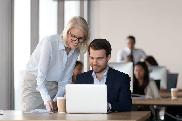 A blonde female manager trains a new bearded male employee