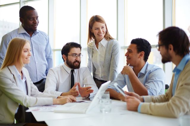 A bearded man with glasses, who is a new manager, meets with his new team.