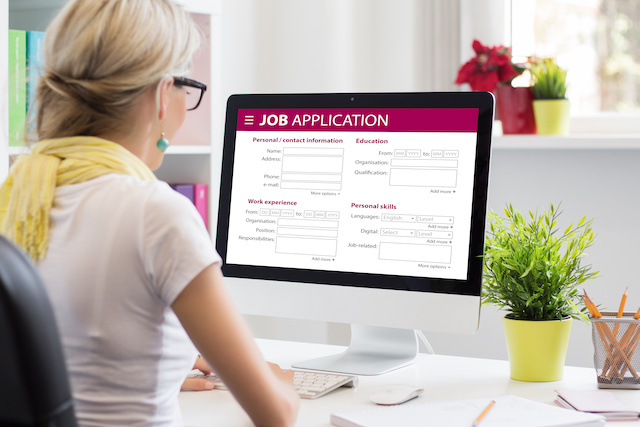 A blonde woman faces her monitor, which displays an online job application form