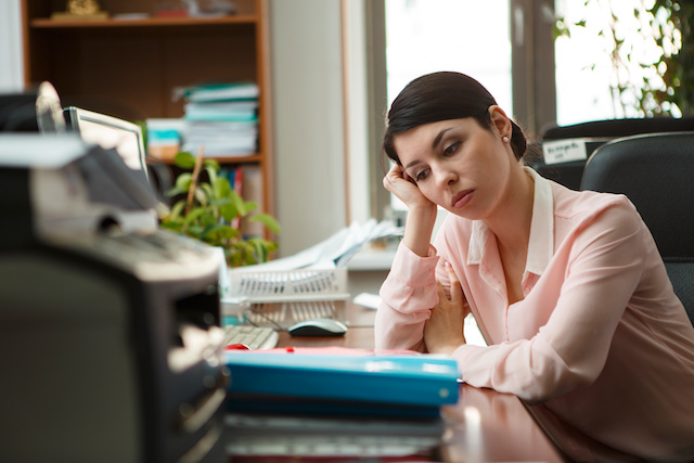 A businesswoman leans her head against her hand on her desk, as she feels unengaged with her work