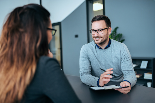 A male manager wearing glasses interviews a female candidate with long hair.