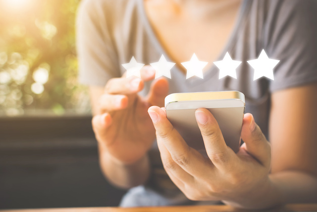 Five stars superimposed over an image of a woman in a t-shirt using her cell phone, representing leaving a company review