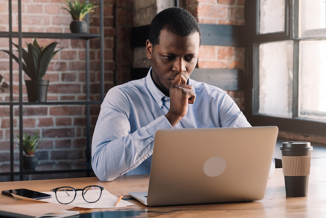 A serious Black businessman sits in front of his laptop.