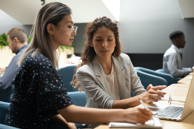 A young Asian woman goes over a project with her female mentor at work