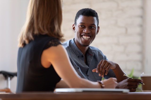 A smiling young Black man is interviewed by a woman