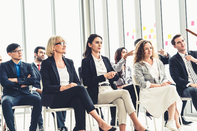 A group of employees sit in rows of seats while attending a workshop