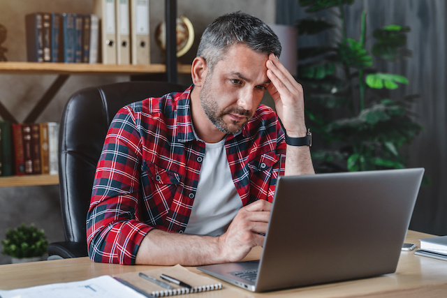 A middle aged male job candidate sits frustrated by his laptop as he waits to hear about a job.