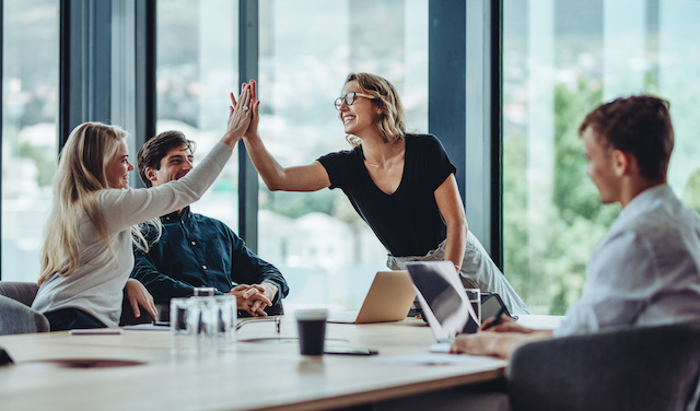 A female employee high-fives a colleague in a team meeting.