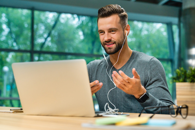 A man wearing earbuds sits at his laptop for a virtual session with his career coach.