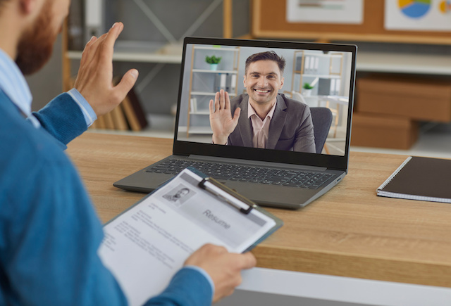 A male hiring manager waves to a male candidate during a remote interview