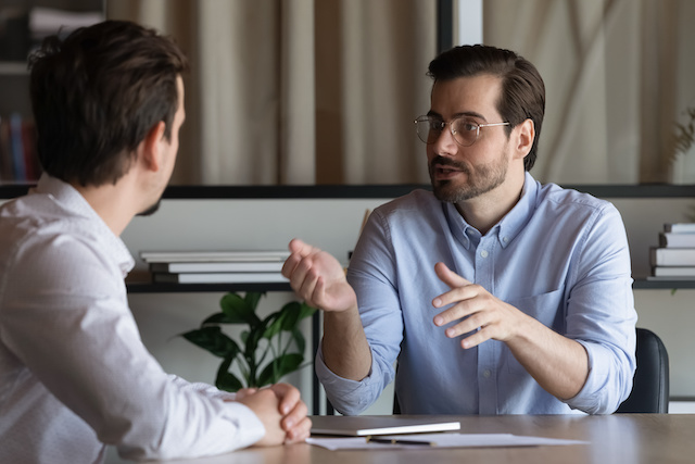 A male manager wearing glasses has a one-on-one meeting with his male employee