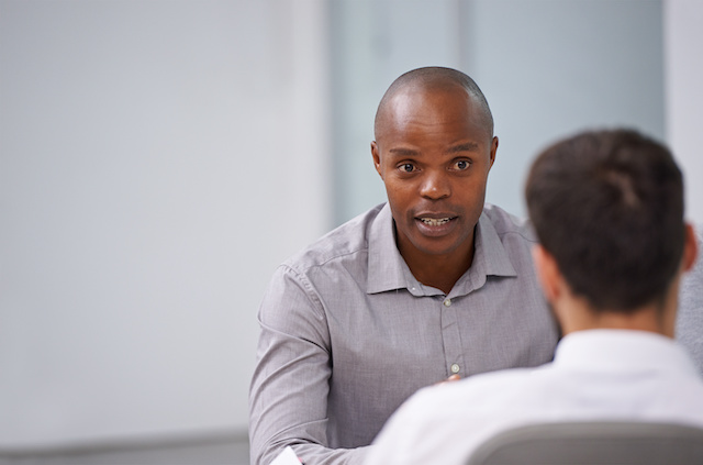 A Black male manager notifies a male employee that he's been laid off.