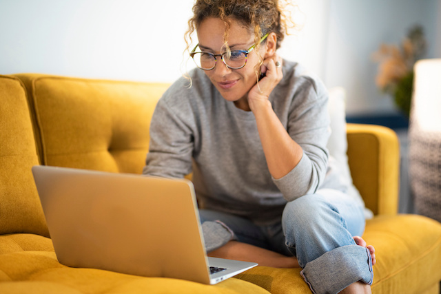 A young woman wearing glasses sits on her sofa while looking at her laptop, representing someone using a top careers site