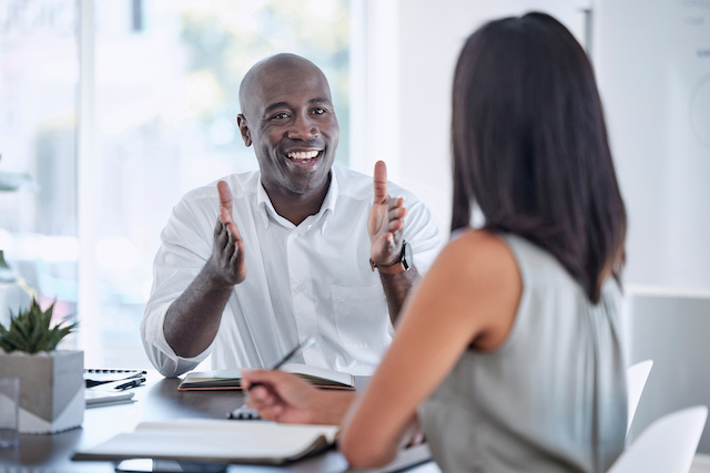 A bald male senior director gives his direct report, a female manager, feedback during her performance review