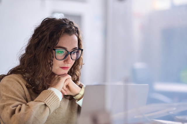 A young woman with glasses sits in front of her laptop