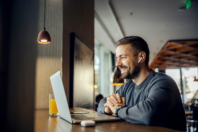 A smiling bearded man has an online meeting on his laptop