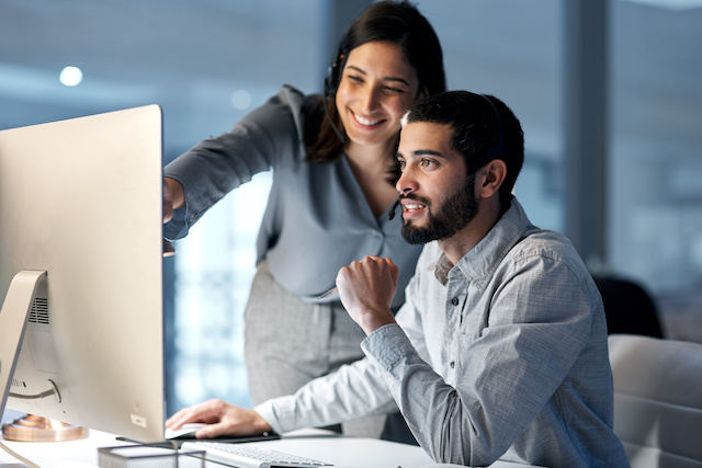 A female manager offers guidance to a male employee at his computer