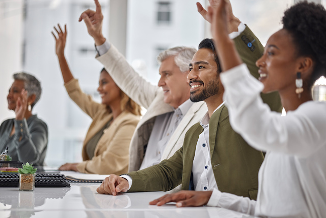 A diverse group of employees raise their hands at a workshop