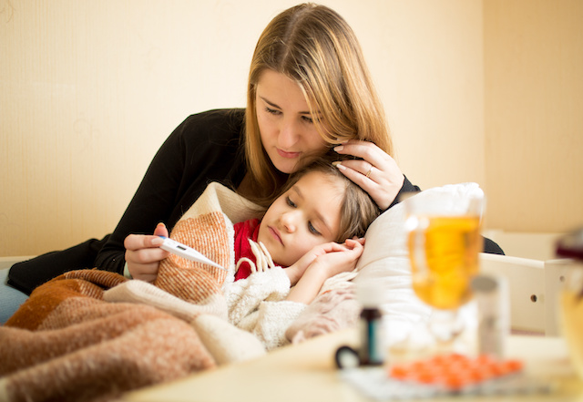 A mother lies in her daughter's bed after taking her temperature 