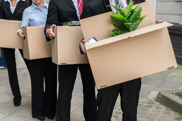 Employees who were laid off exit their office building with cardboard boxes of their belongings