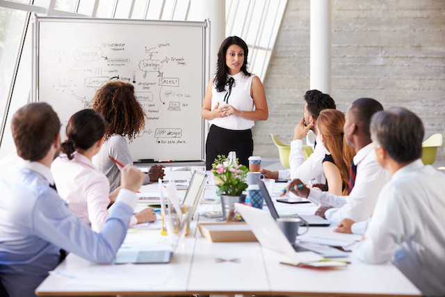 A female director leads her diverse team through a process meeting.