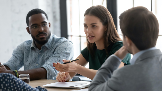 A young female employee shows qualities of an emerging leader by initiating a discussion to solve a business problem with her male colleagues.