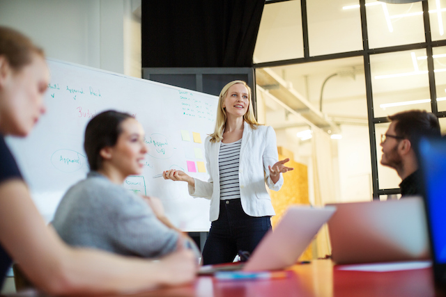 A female employee gets practical experience in communication by making a presentation to team members in order to develop this soft skill.