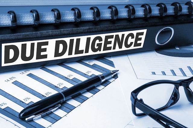 A binder labeled "Due Diligence" sits atop reports near a pair of glasses