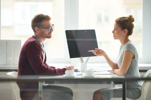 A young, female HR director meets with a male employee to notify him that he's been laid off.