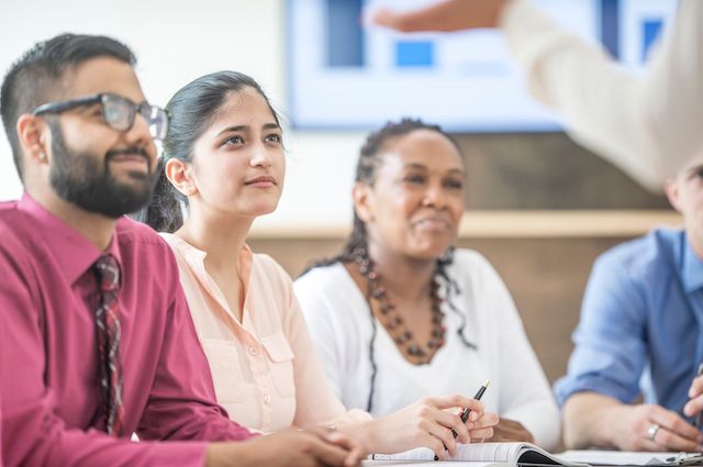 A multicultural group of new managers sit in a meeting about first-time manager training.