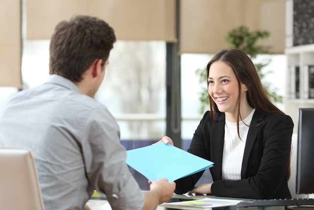 A female manager hands her male employee a file with his performance review