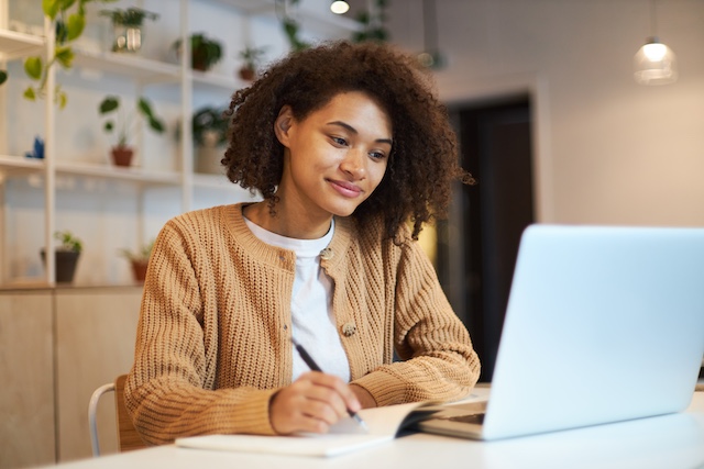 A young Black woman works at her laptop at home.