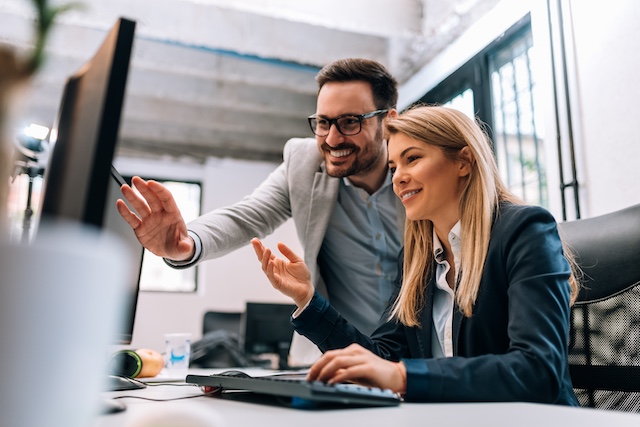 A male manager trains his female employee at her desk