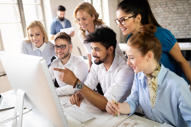 Young male employee explains work to his colleagues using his monitor