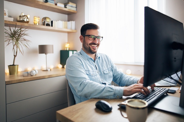 A smiling man works at his desk in his home office