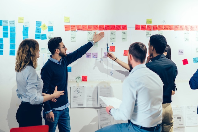 A diverse team of employees brainstorms using sticky notes on a wall