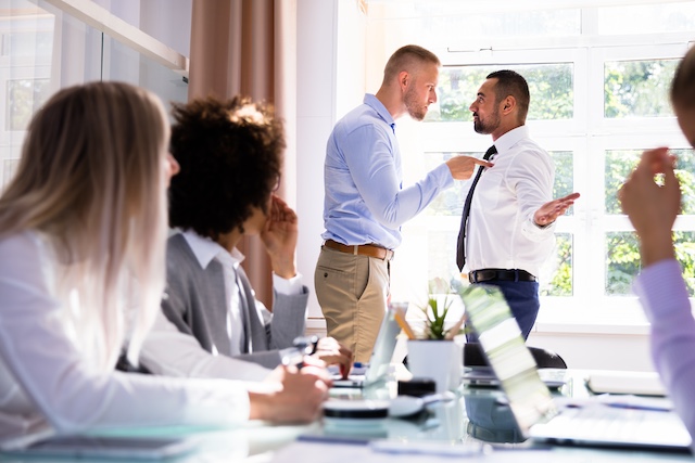 A man bullies a male colleague during a business meeting